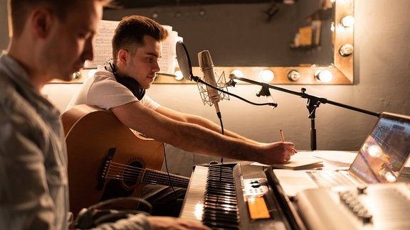 Zwei Personen sitzen an  Keyboard und Mikrofon.