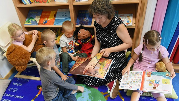  In der Sprach-Kita Bummi liest die Klinische Diplomwissenschaftlerin und Sprachfachkraft Josefin Heinze mit vier-und fünfjährigen Kindern in einer kleinen Bibliothek ein Buch.