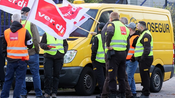 Teilnehmer eines Streiks stehen vor einer Niederlassung von Prosegur in Hamburg an einem Geldtransporter. 