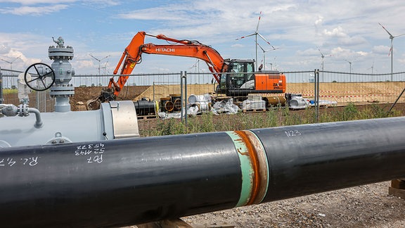 Die Rohre einer künftigen Wasserstoffleitung liegen vor der Kulisse eines Windparks.