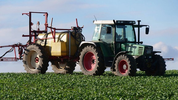 Auf einem Acker bringt ein Landwirt mit Hilfe einer Ackerspritze Pflanzenschutz gegen Schädlinge auf Winterweizen aus