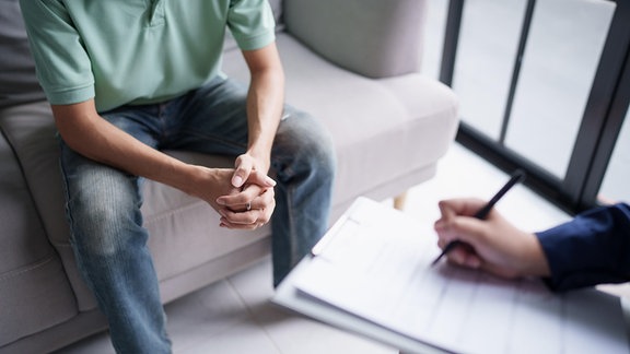 Inszeniertes, ausschnitthaftes Foto einer Therapiesitzung in der sich zwei Personen gegenüber sitzen.