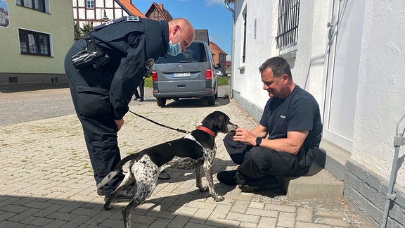 Zwei Polizisten mit einem Personensuchhund/Mantrail-Hund auf einer Treppe.