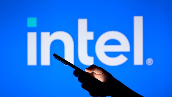 Symbolfoto: Eine Hand hält ein Mobiltelefon vor ein Intel-Logo.