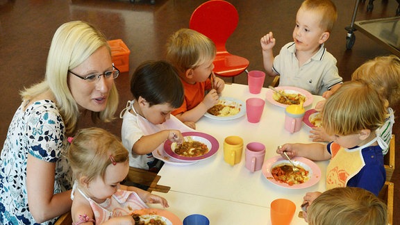 Krippenkinder (1,5 bis 3 Jahre) sitzen am Mittwoch, den 24.07.2013 in der BBW-Kindertageseinrichtung "forum thomanum" in Leipzig mit Diplom-Sozialpädagogin Anne Schröder beim Mittagessen. Neben der Leiterin kümmern sich neun pädagogische Mitarbeiterinnen und Mitarbeiter sowie fünf Sprachassistentinnen und Sprachassistenten um die 18 Krippen- und 82 Kindergartenkinder. 