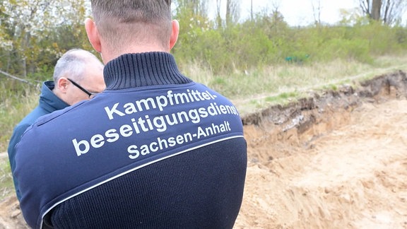 Zwei Personen vom Kampfmittelbeseitigungsdienst neben einer Sandgrube. 