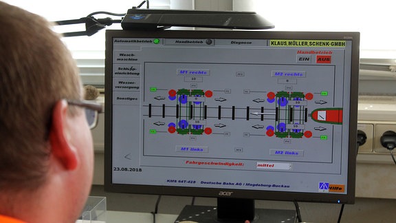 ein Mann schaut auf einen Bildschirm mit einer schematischen Darstellung einer Zugwaschanlage