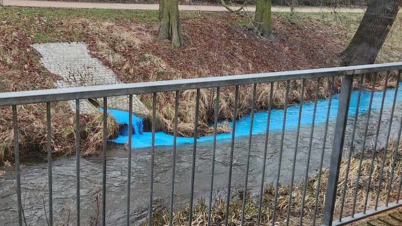 Der Blick in einen Kanal in den aus einem Rohr blaube Farbe läuft. 