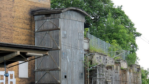 Blick auf einen alten holzumschalten Lastenaufzug an einem dreigeschossigen Bahnhofsgebäude.