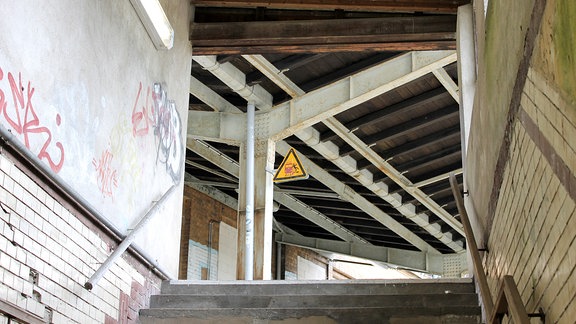 Blick aus einem Tunnel hinaus auf ein Bahnsteigdach mit rostigen Trägern.