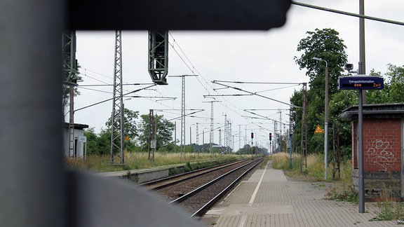 Entlang eines gepflasterten Bahnsteigs führt eine zweigleisige elektrifizierte Bahnstrecke. 