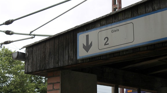 An einem Dach hängt ein blau-weißes Hinweisschild, ein Pfeil weist den Weg zu Gleis 2.