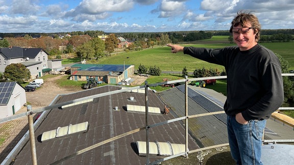 Ein Mann auf einem Dach zeigt über zahlreiche Häuser, die mit Solarmodulen bedeckt sind.