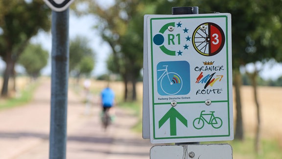 Ein grün umrandetes Schild weist auf mehrere Fahrradrouten hin, die alle demselben Weg folgen