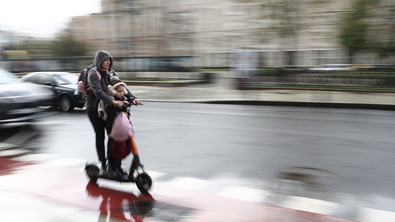 Zwei Menschen fahren auf einem E-Scooter.