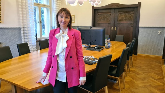 Eine junge Frau mit rosa Jacket steht in einem repräsentativen Besprechungsraum.