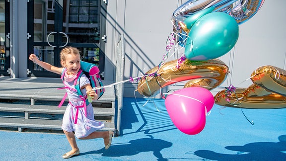 Fröhliches kleines Mädchen mit Schulranzen und Ballons