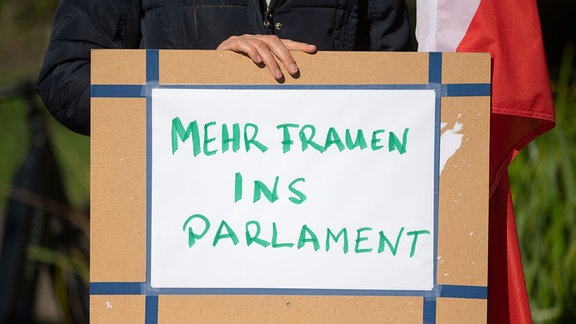 Teilnehmerin einer Kundgebung steht hinter einem Plakat mit der Aufschrift "Mehr Frauen ins Parlament"