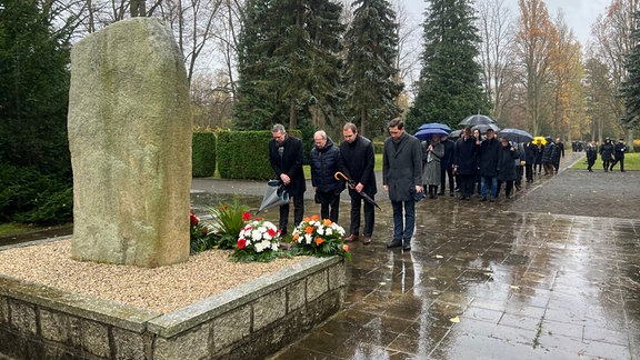 Menschen stehen vor einem Gedenkstein auf dem Halberstädter Friedhof.