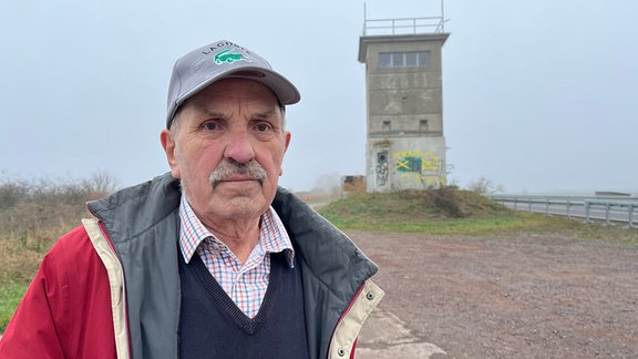 Ein älterer Mann im Vordergrund, im Hintergrund ein alter Wachturm.