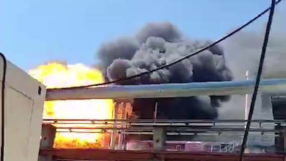 Auf einem Dach einer Halle sind ein Feuerball und schwarzer Rauch zu sehen