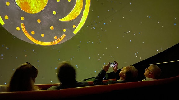 Vier Personen schauen sich in einem Planetarium den Nachthimmel mit der Himmelsscheibe von Nebra an.