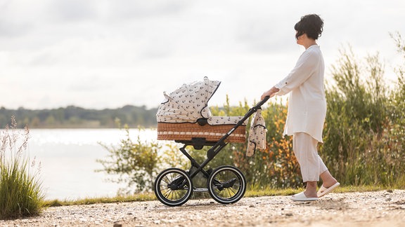 Eine Frau mit einem Kinderwagen an einem See.