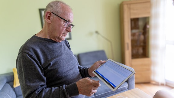 Ein älterer Mann schaut auf einen Tablet-Computer