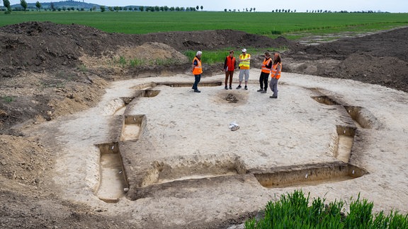 Auf einem Feld bei Nauendorf stehen Personen im Grundriss einer 6000 Jahre alten Totenhütte. 