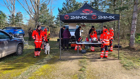 Mehrere Menschen in oranger Rettungsmontur stehen am Waldrand