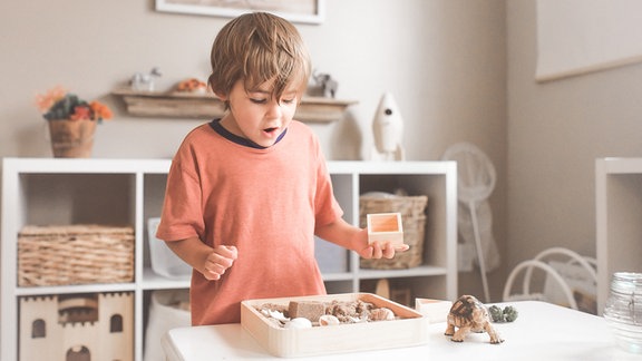 Ein Junge im Kindergartenalter spielt stehend an einem Tisch.