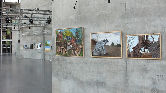 In einem lichtdurchfluteten Foyer hängen an Betonwänden - wie in einer Galerie - verschiedene Gemälde iund Fotografien dicht beieinander