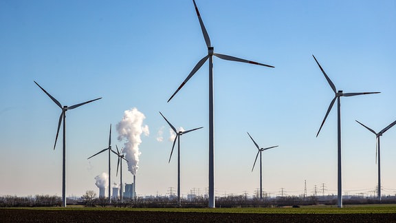 Der Schornstein und die Kühltürme des Braunkohlekraftwerks Schkopau dampfen hinter einem Windpark.