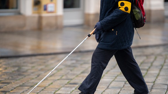 Person mit Blindenarmbinde und Blindenstock läuft.