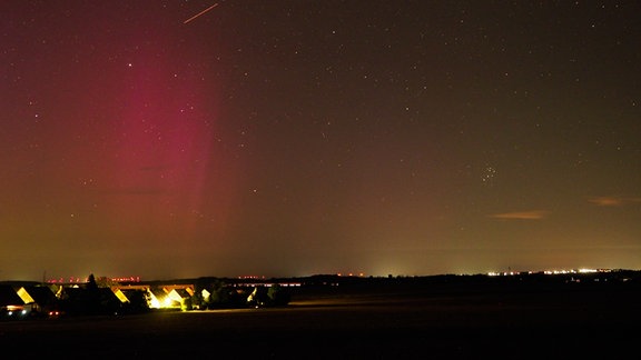 violette Polarlichter und eine Sternschnuppe an einem Nachthimmel