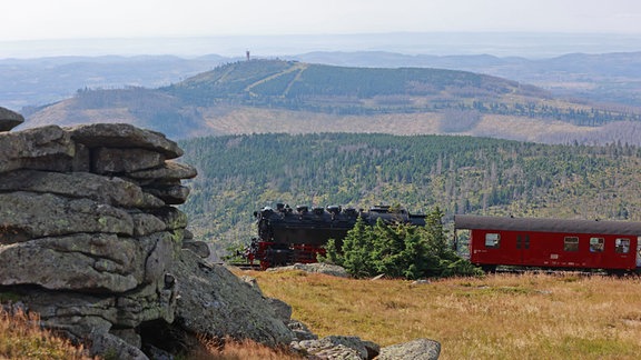 Ein Zug der Harzer Schmalspurbahn HSB fährt hinter der Teufelskanzel auf dem Brocken entlang. 