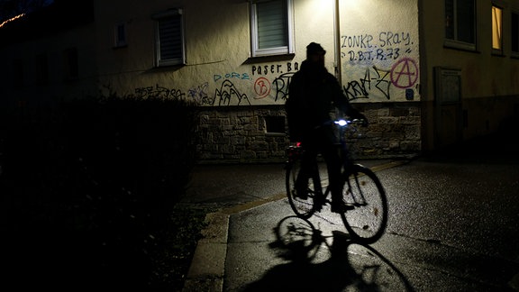 Ein Radfahrer ist 2020 im Dunklen unterwegs und biegt um ein mit Tags beschmiertes Hauseck.