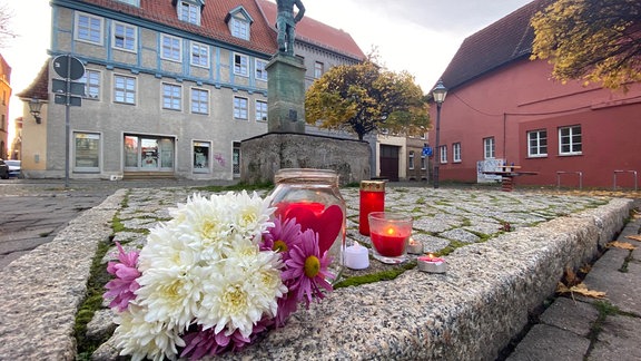 Auf einem Marktplatz liegen Blumen und Kerzen.