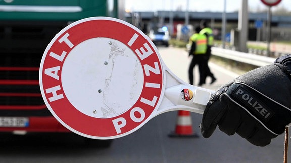 Ein Polizist stoppt mit seiner rote Kelle einen LKW. 