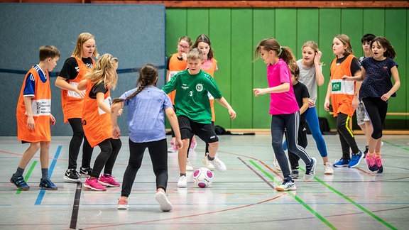 Kinder spielen in einer Sporhalle Fußball.