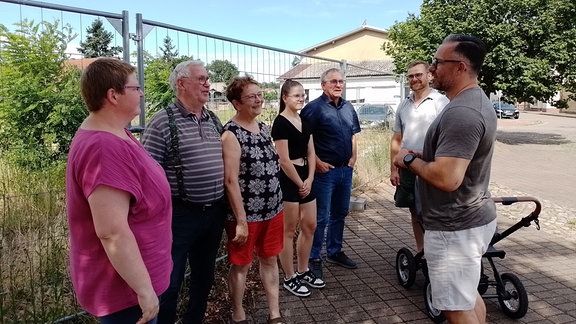 Mehrere Frauen und Männer unterhalten sich vor einem Bauzaun