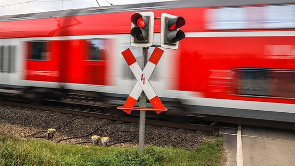 Ein Zug fährt an einem Bahnübergang mit Halbschranke vorbei.