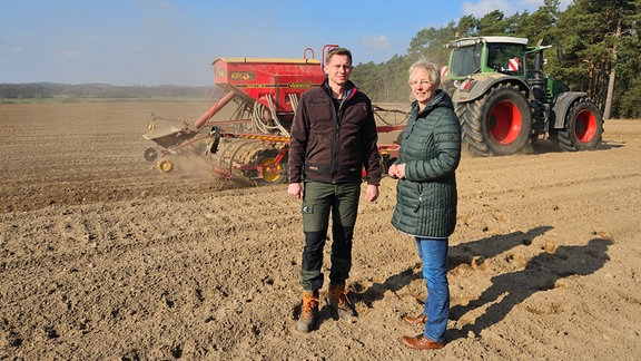 Eine Frau und ein Mann vor einem Traktor auf einem Acker