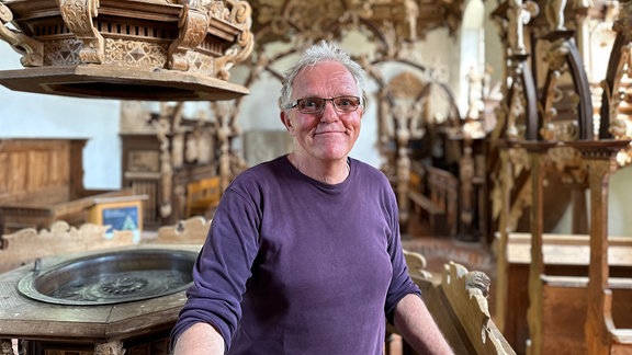 Ein Mann mit violettem Shirt steht inmitten einer mit Holzelementen ausgestatteten Kirche