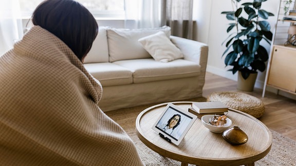 Eine Frau auf einem Sofa spricht online mit einer Ärztin.