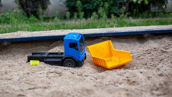 Einige alte und kaputte Plastikspielzeuge liegen im Sand eines Spielplatzes. 