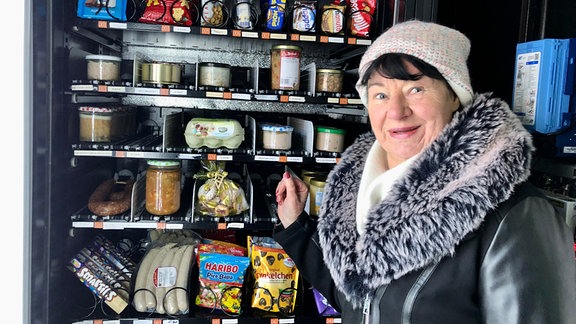 Eine Frau mit Mütze und Jacke steht an einem Automaten.