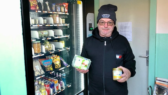 Ein Mann steht mit Honig und Eierpackung vor einem Automaten.