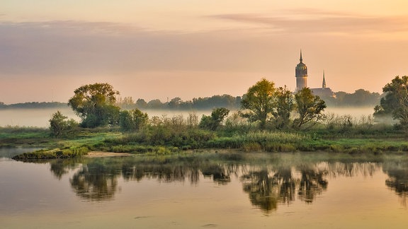 Sonnenaufgang an der Elbe mit Blick auf die Schlosskirche in Wittenberg