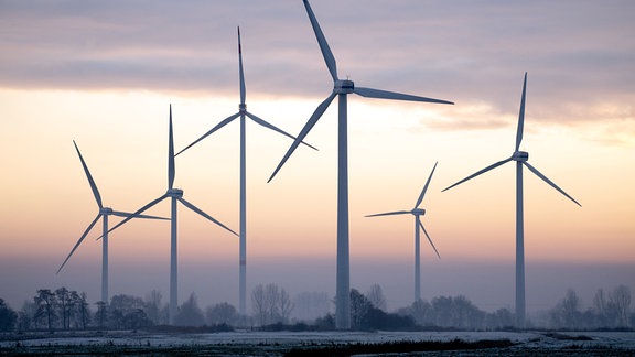 Windkraftanlagen stehen bei winterlichem Wetter vor dem sonnigen Abendhimmel